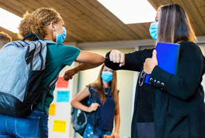 high school student elbow bumping teacher, both wearing masks